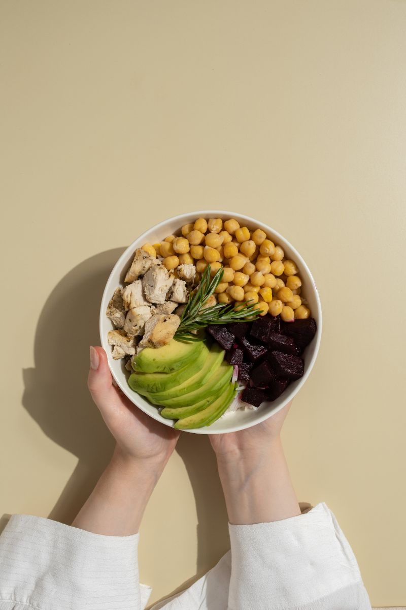 hands holding a bowl of avocado, chickpeas, beets and chicken