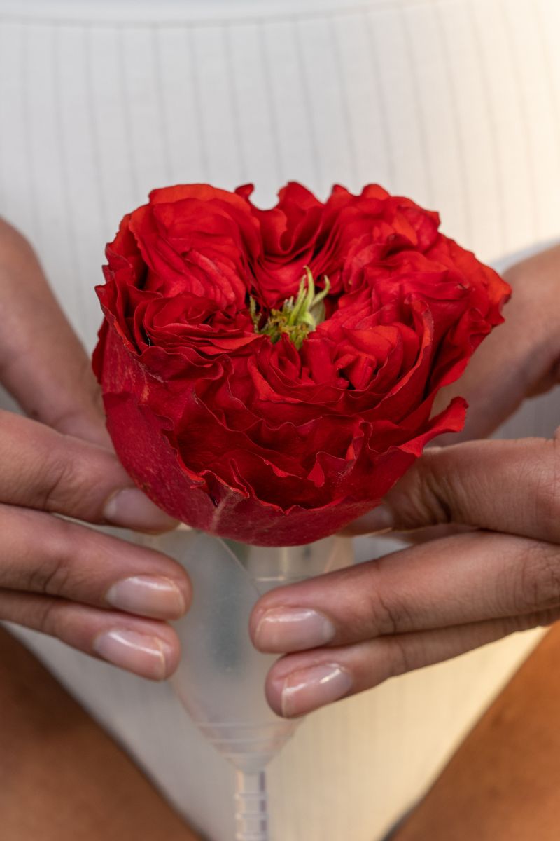 a person holding a red flower inside a menstrual cup