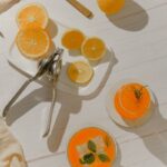 two cocktails next to a cutting board with sliced oranges and a citrus press