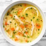 a bowl of lemon chicken soup topped with fresh herbs