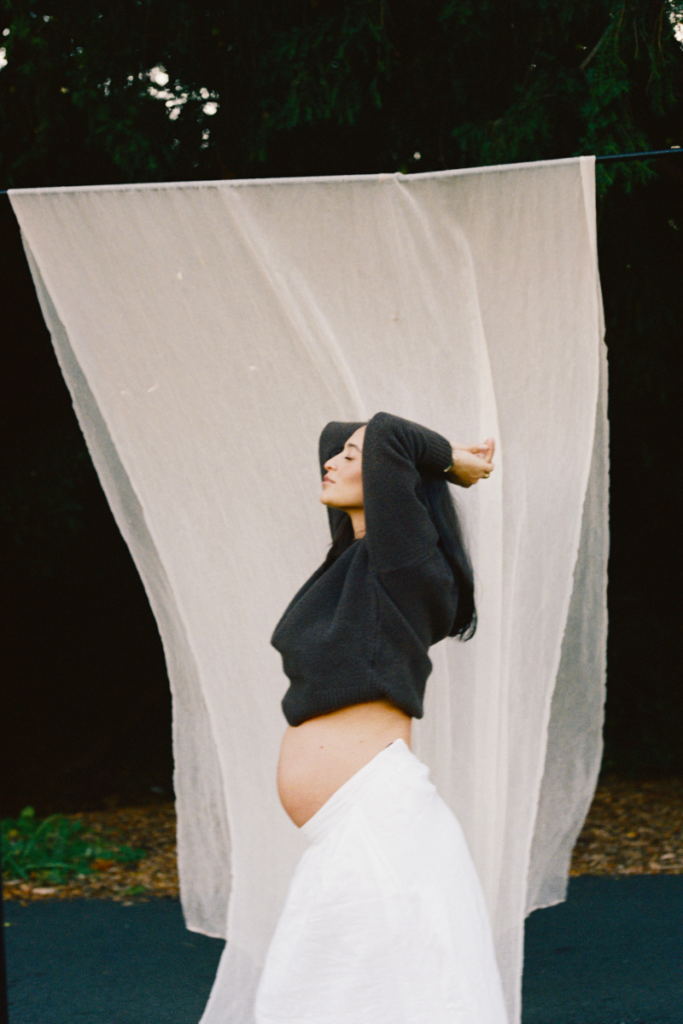 Holistic Fertility Support and Pregnancy Wellness Pregnant woman standing outdoors in front of a soft fabric backdrop, representing fertility support, hormone health, and pregnancy wellness.