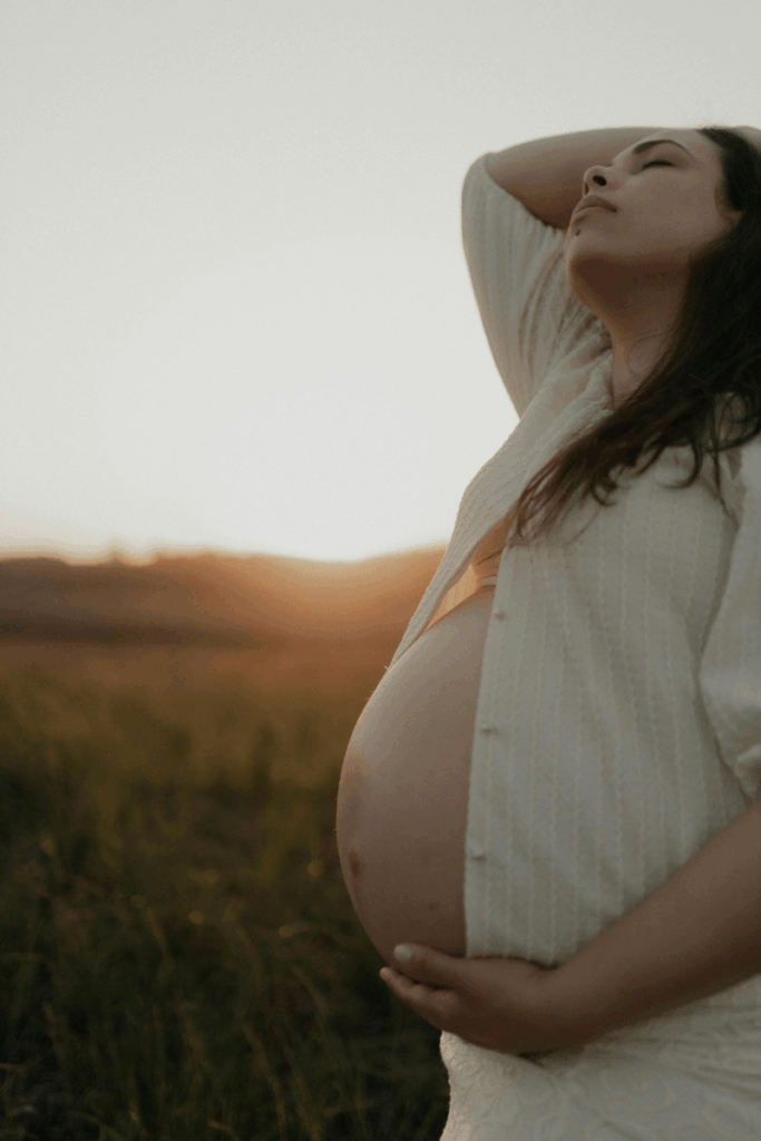 A pregnant woman holding her belly in a field.