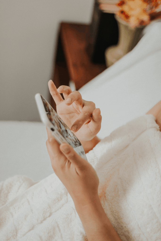 A woman's hands holding a phone while scrolling in bed.