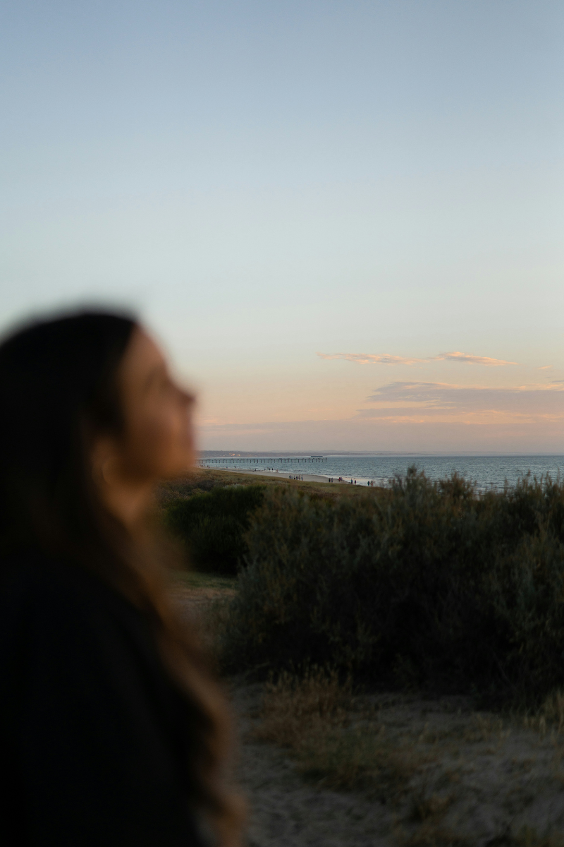 Woman gazing upward at a sunset ocean view, representing emotional release and healing through EFT tapping