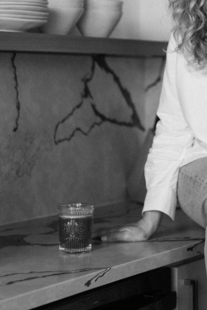 Black-and-white photo of a woman standing at a kitchen counter beside a glass.